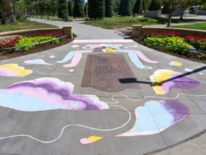 A sidewalk mural of abstract people huddling together and clouds next to a park
