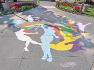 A sidewalk mural of multi-coloured silhouettes of people next to a park
