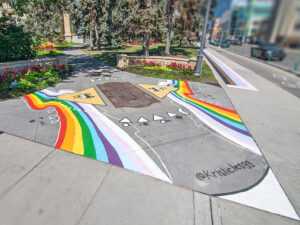 A sidewalk mural of Indigenous symbols and rainbows next to a park