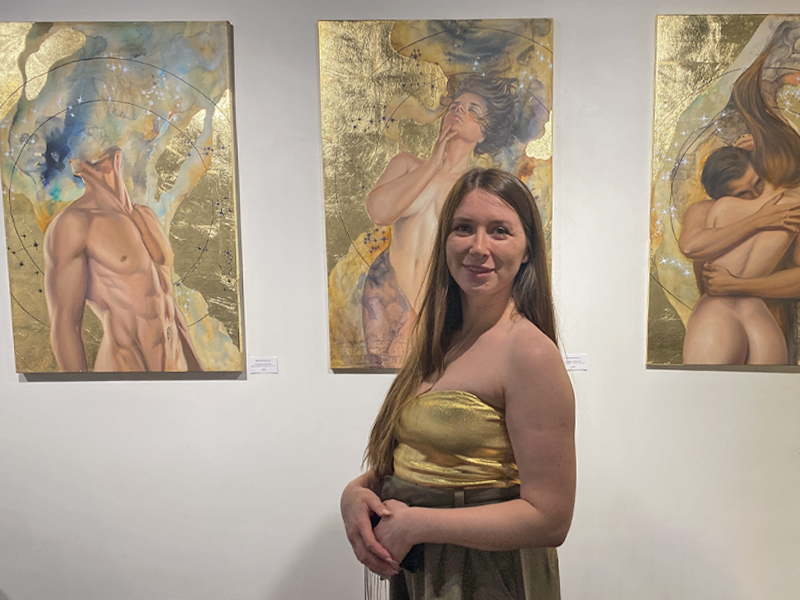 Ukrainian artist Maria Mykhalap stands in front of three her paintings, part of a series of nudes.