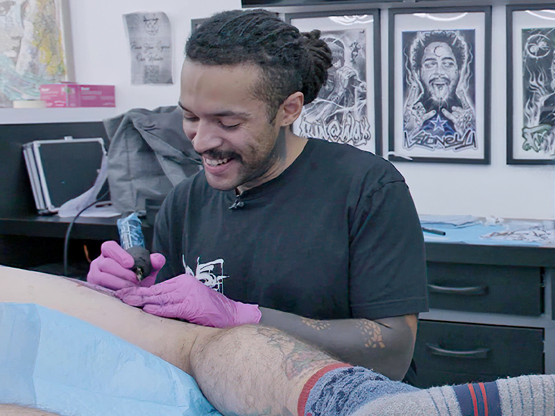 An image of tattoo artist Mario Griffiths tattooing the leg of a client