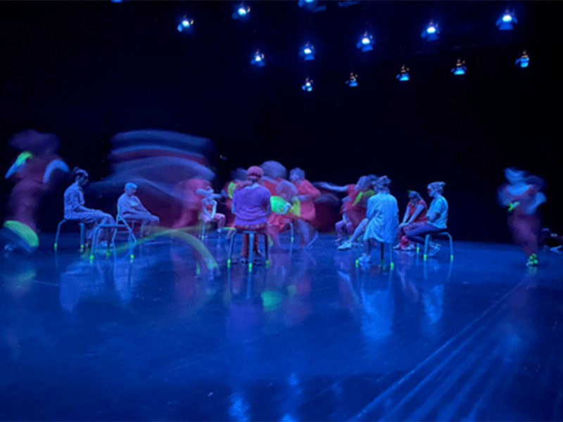 An image of dancers sitting/performing in blue light