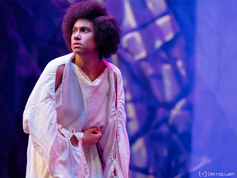 An actor in white robes against a purple background