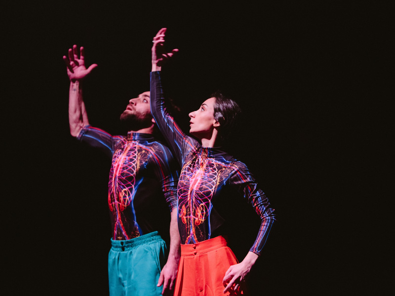 An image of Mario Obeid and Zaria Rajha mid performance earch wearing multi-coloured skeletal body suits and a pair of shorts