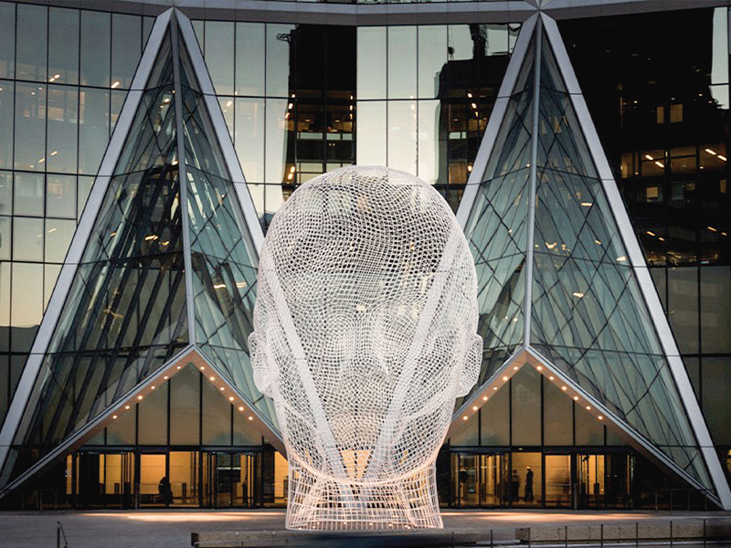 A photo of artist Jaume Plensa's bent-wire sculpture Wonderland, aka the giant head, taken in front of The Bow office tower.