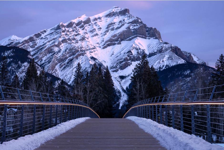Photograph of a footbridge in the foreground and a mountain in the background in Banff, Alberta
