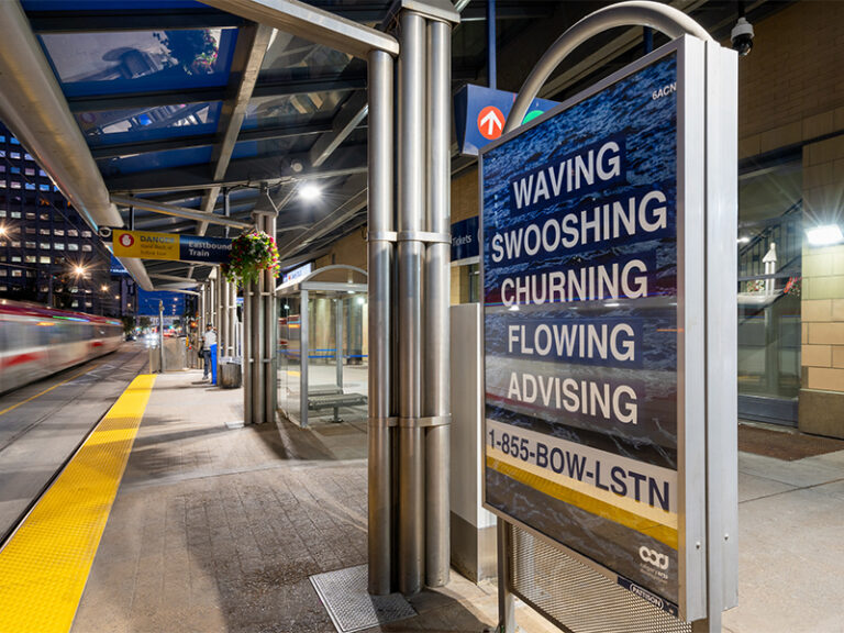 A digital poster, shown at an LRT station at night, with a background of flowing water and text that reads Waving, Swooshing, Churning, Flowing, Advising. 1-855-Bow-Lstn.