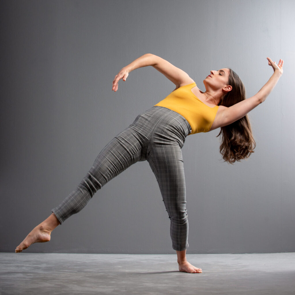 Female performer in a wide dance pose before a grey background.