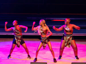 Three dancers perform on stage from Woezo Africa Music and Dance Theatre