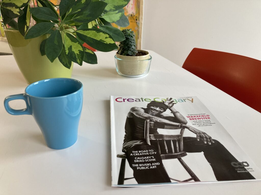 A copy of Create Calgary. magazine on a table with a cup and a plant