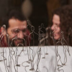 Artist collective Incipio Modo in soft focus behind a wire artwork.