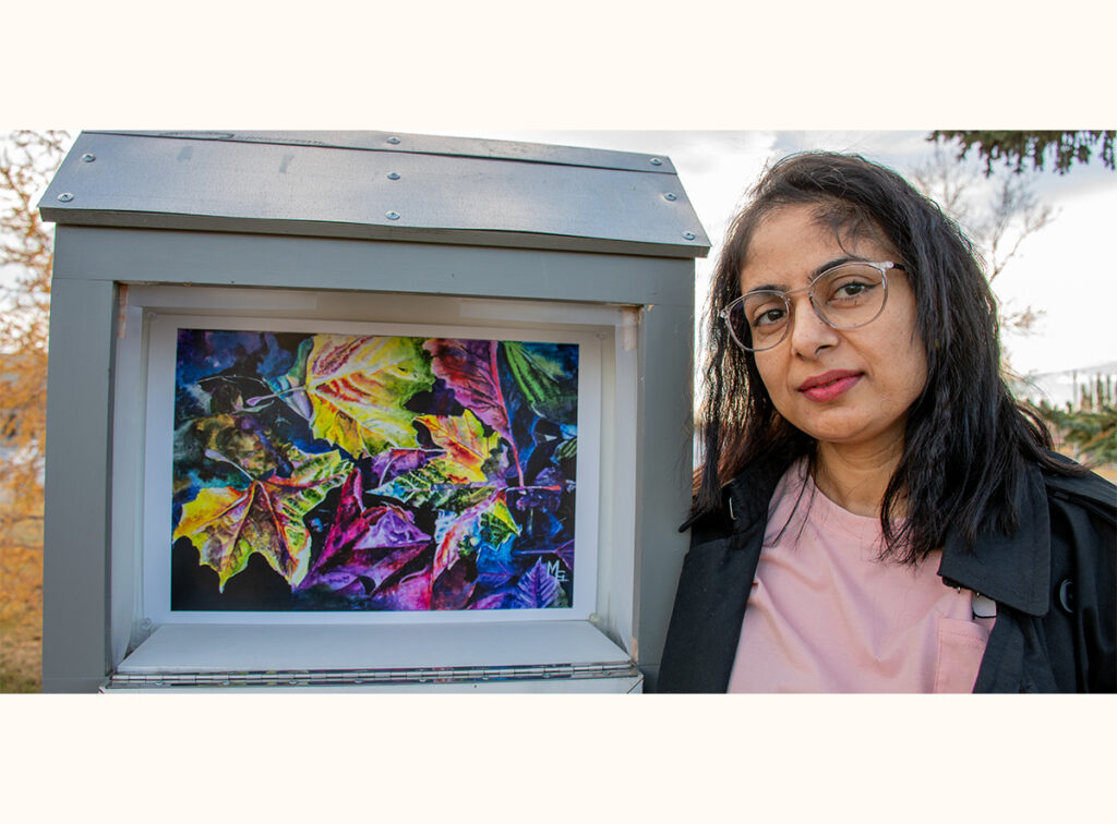 Meenakshi Girdhar stands beside her mini gallery, showcasing colourful artwork of autumn leaves.