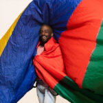 Tyson Bankert smiling while wrapping himself in a big colourful flag.