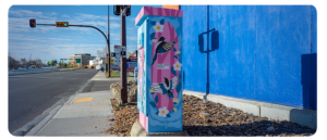 A utility box painted with colourful birds and flowers at a street intersection.