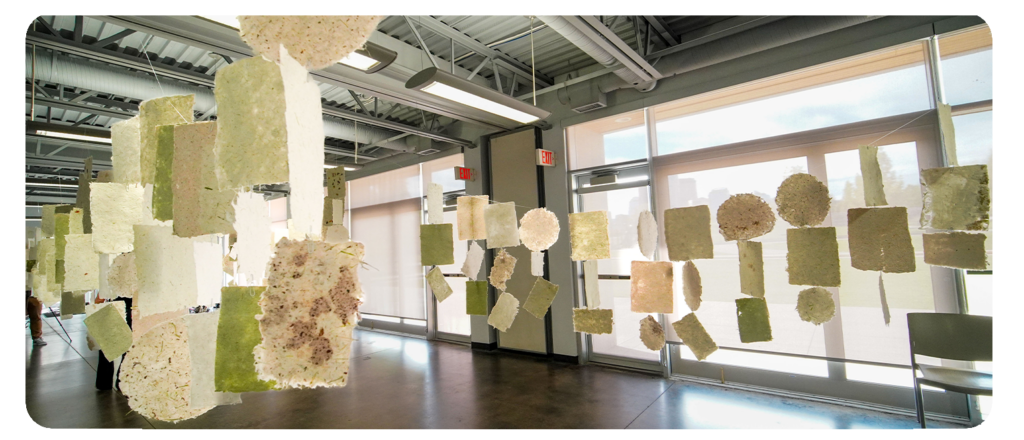 Handmade paper sheets hang from the ceiling in an indoor space.