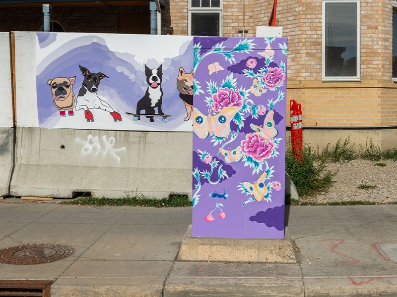 A purple utility box decorated with vibrant butterflies and flowers near a mural of a dog and a skateboarder.