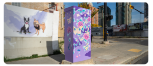 A purple utility box decorated with vibrant butterflies and flowers near a mural of a dog and a skateboarder.