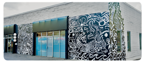 A strip mall building with public art mural wrapping the one-story building