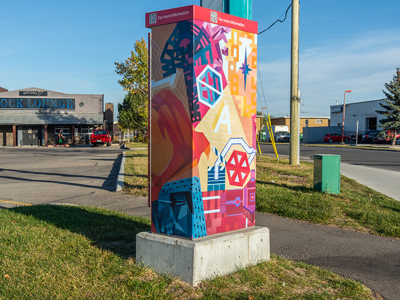 A utility box in a parking lot, painted with colourful shapes and abstract designs.