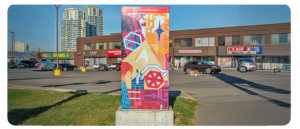 A utility box in a parking lot, painted with colourful shapes and abstract designs.