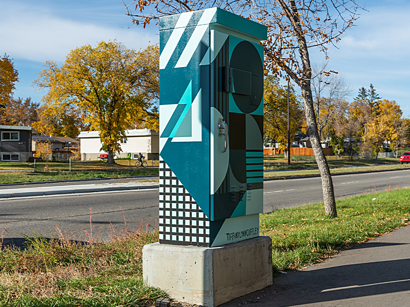 A utility box painted with shapes in shades of blue, teal, and black, with circles, stripes, and rectangles.