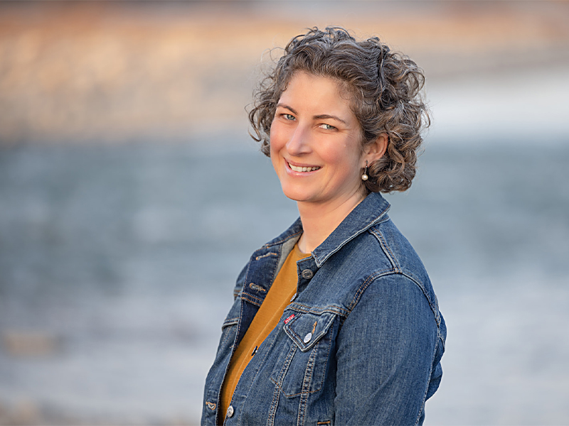 Geraldine Ysselstein standing against the backdrop of a river wearing a denim jacket