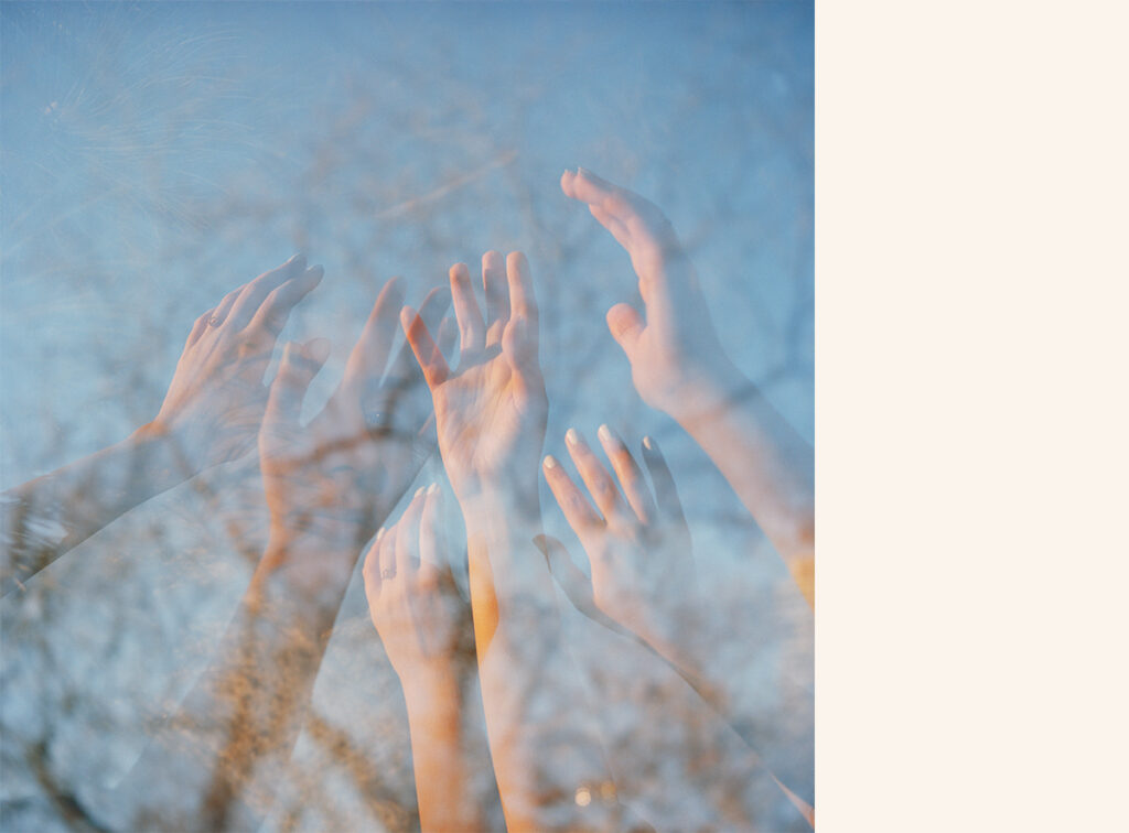 An image of multiple hands reaching upwards, layered against a blue sky.