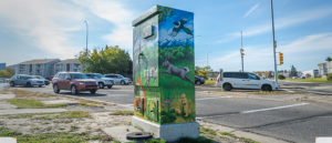 A utility box painted with a nature scene, featuring animals like a rabbit, fox, and magpie, set against a mountainous background.