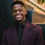 KTheChosen standing wearing a purple suit against a background of concrete steps