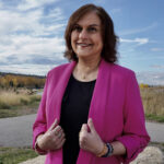 Kelly Kaur wearing a pink blazer standing outdoors against a prairie backdrop