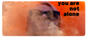 A person wearing large black sunglasses is partially obscured by swirling white smoke. Bold black text on the top right reads, “you are not alone.”