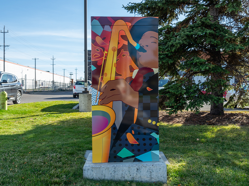 A utility box painted with an abstract design of a musician playing a saxophone, with vibrant colours and shapes in the background.