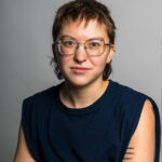 Misha Storkova wearing a black top sitting against a grey backdrop