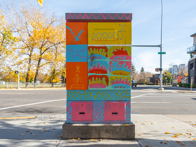 A colourful utility box with abstract designs and the phrase "We choose our joy,".