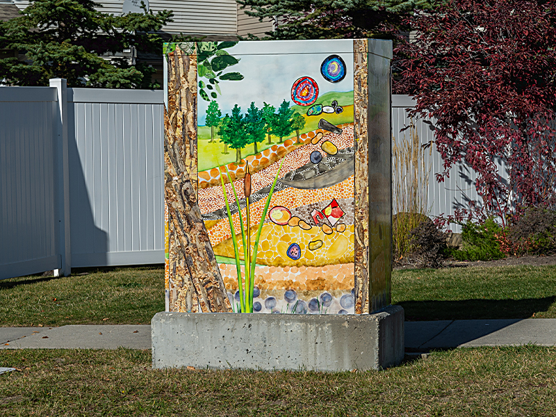 Utility box painted with a nature scene featuring trees, hills, stones and soil.