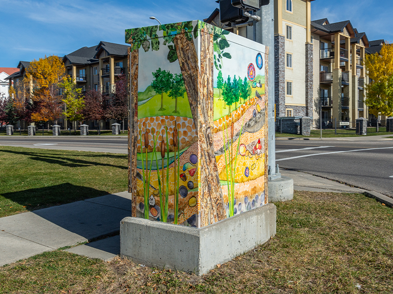 Utility box painted with a nature scene featuring trees, hills, stones and soil.