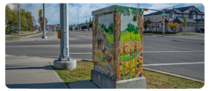 A utility box painted with a nature-inspired mural featuring trees, plants, rocks, and a scenic landscape.