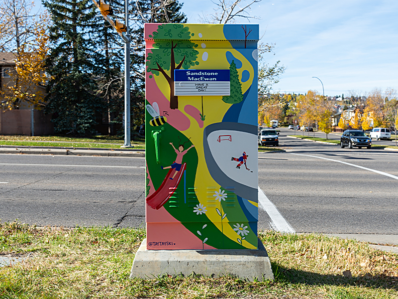 Utility box painted with children playing sports, a slide, and various outdoor scenes.