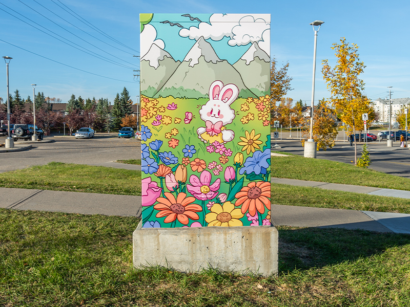 Utility box painted with a cartoon style scene of a bunny in a flower field, with mountains and a bright sky in the background.