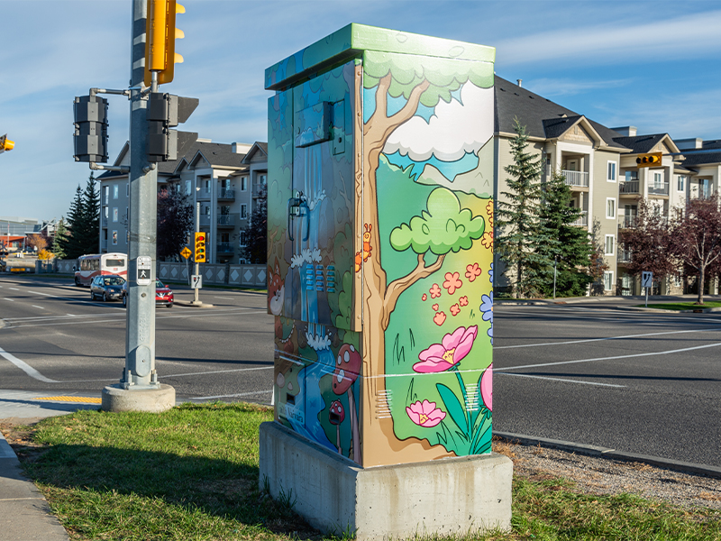 Utility box painted with a nature scene featuring trees, flowers, and a waterfall.