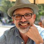 Stephen Duncombe smiling wearing a hat and resting his chin on his hand