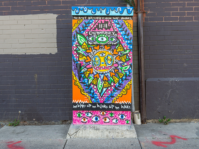 Utility box with a vibrant, sun design, eyes, and "Wake Up" text.