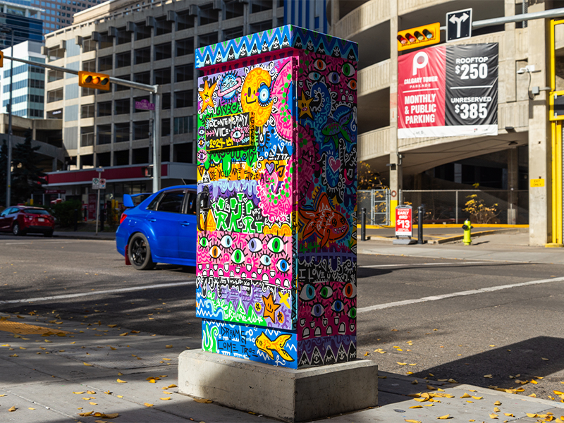 Utility box featuring colourful shapes, faces, and graffiti.