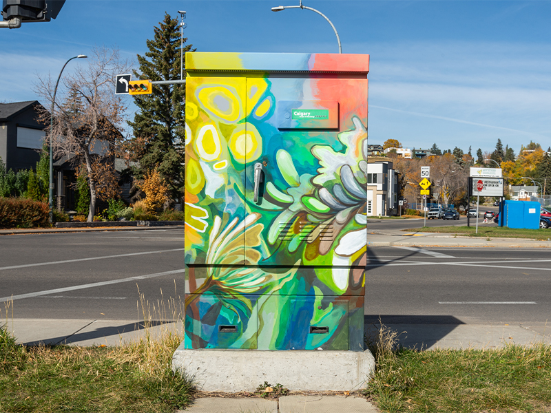 Utility box painted with a vibrant mix of floral and leafy patterns in yellow, green, and blue.