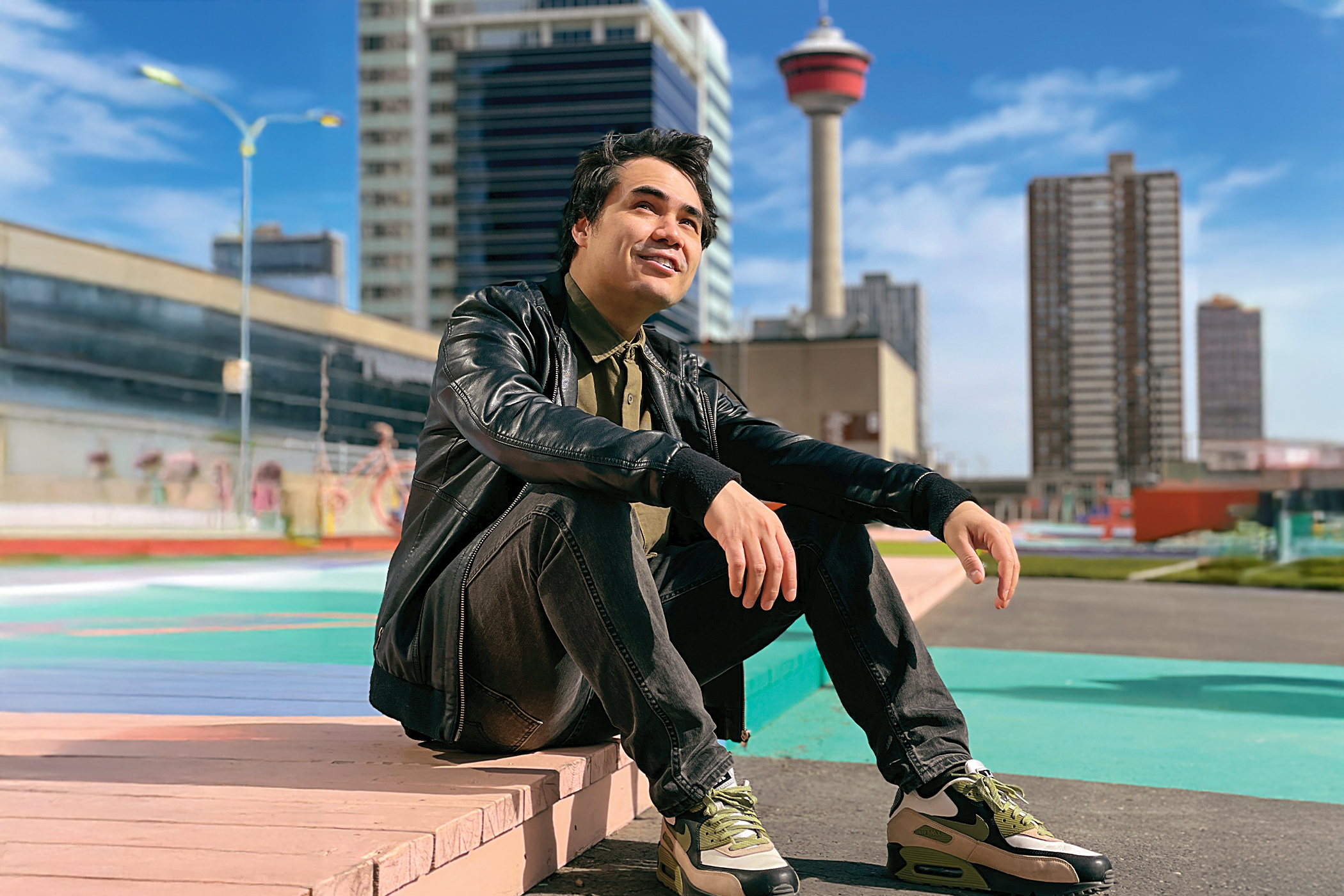 Artist Jarett Sitter sitting on a sidewalk in front of a backdrop of the city