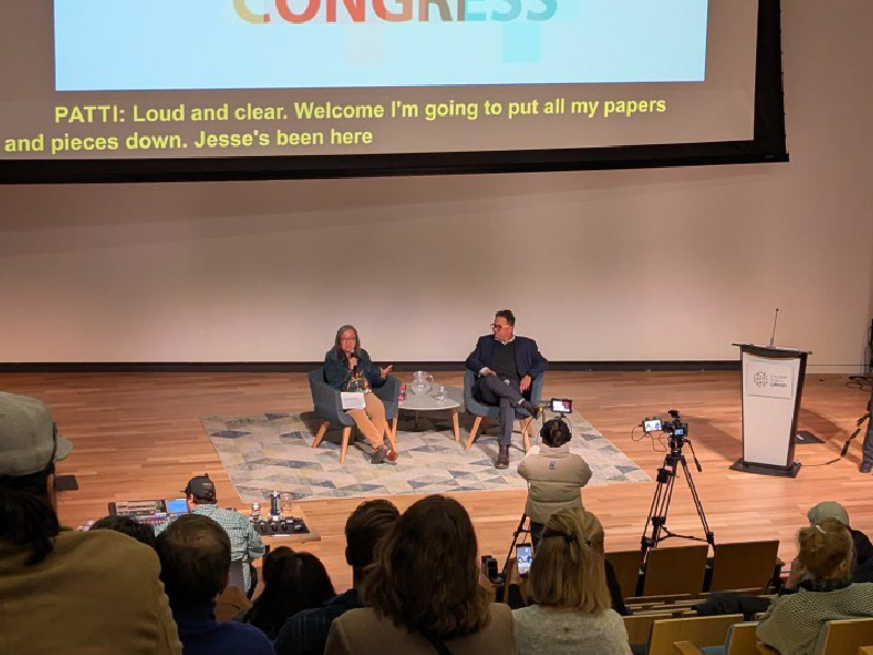 Patti Pon and Jesse Wente seated in chairs onstage, with the audience in the foreground.