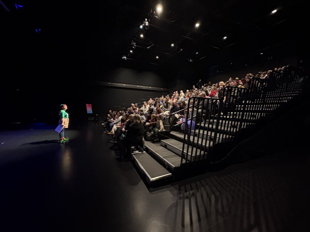 Photograph of a theatre at YMCA Calgary location unknown with audience members watching a performer