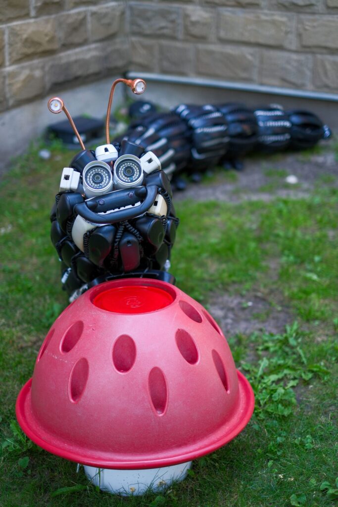A sculptural installation representing a caterpillar or bug near something that resembles a red coloured mushroom