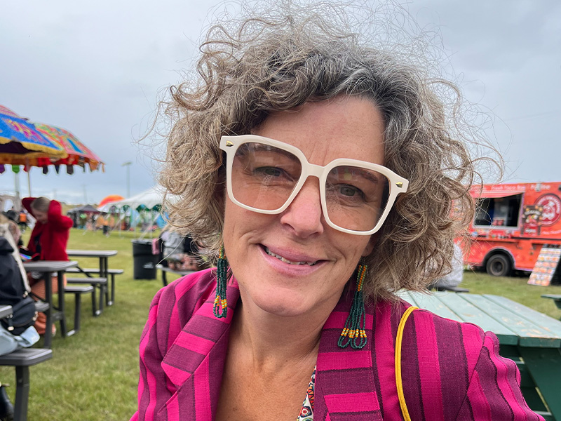 Angie Davis wearing bold pink eyeglasses wearing a pink striped blazer sitting at what appears to be an outdoor festival