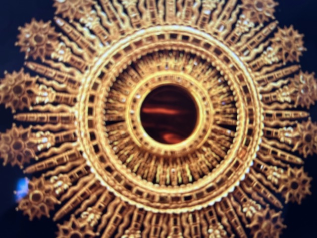 A very intricate and ornate golden decoration. It sort of feels like a sun and has seemingly an eye in the middle.